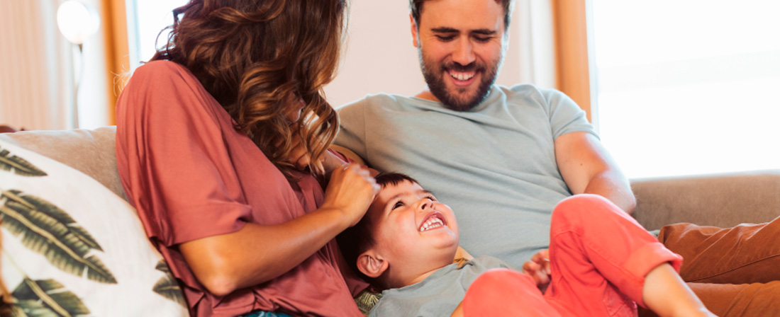 Madre y padre sentados en un sofá jugando con su hija pequeña