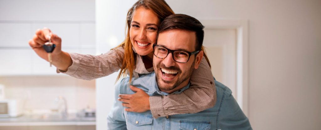 Pareja en actitud feliz y cariñosa mientras sujetan las llaves de una vivienda