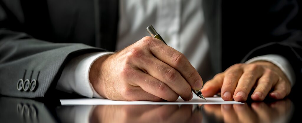 Señor en traje firmando un papel con bolígrafo