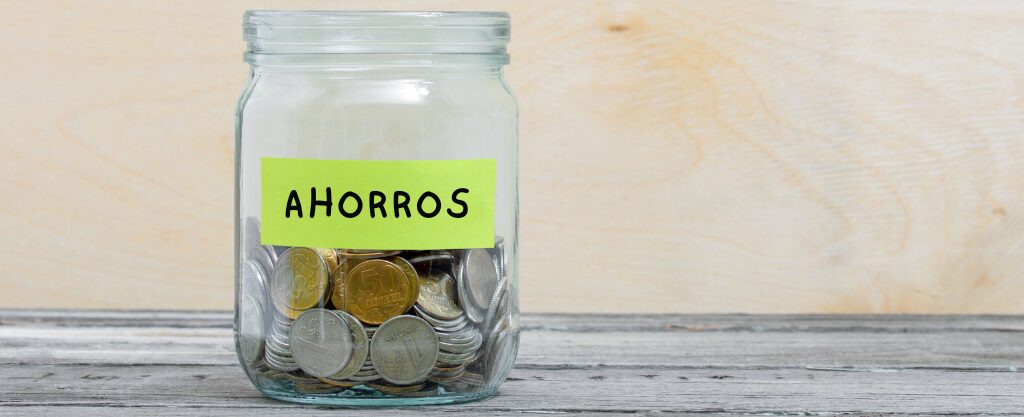 Tarro de cristal con monedas dentro y una etiqueta escrita a mano en la que pone "Ahorros"