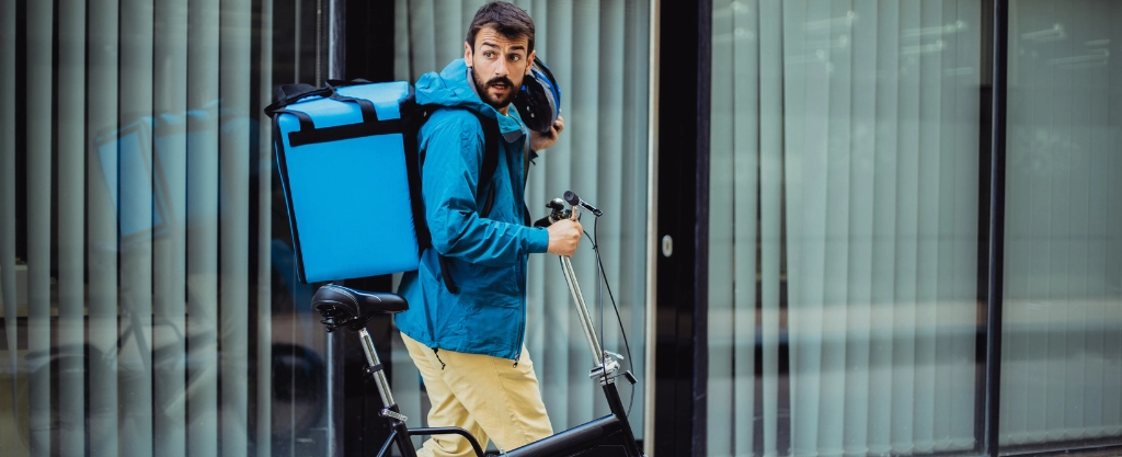 Hombre trabajando a media jornada como repartidor a domicilio con una bicicleta y una mochila de reparto azúl