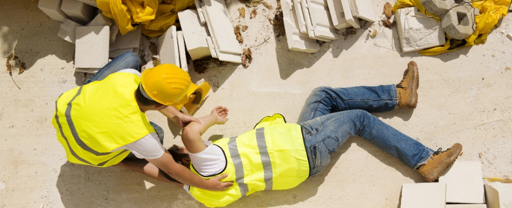 Un operario de obra ayudando a otro que ha sufrido un accidente laboral
